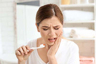 tooth decay woman trying to brush her teeth but realizing she has tooth decay
